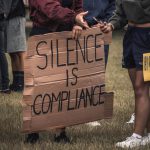 Protest sign that reads, "silence is compliance"