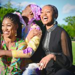 Three black women laughing and embracing.